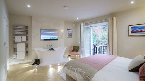 A modern bedroom with a large bed, a bathtub, and a balcony with a view.