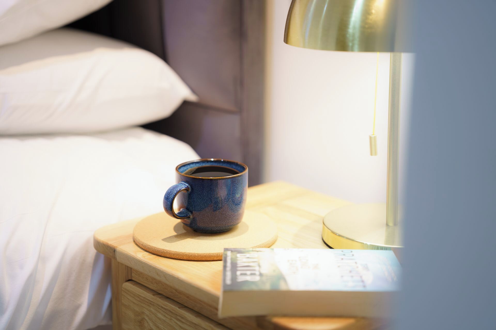 A wooden bedside table with a ceramic mug and a book.