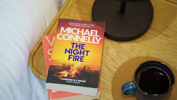 A book titled "The Night Fire" by Michael Connelly on a bedside table next to a cup of coffee.