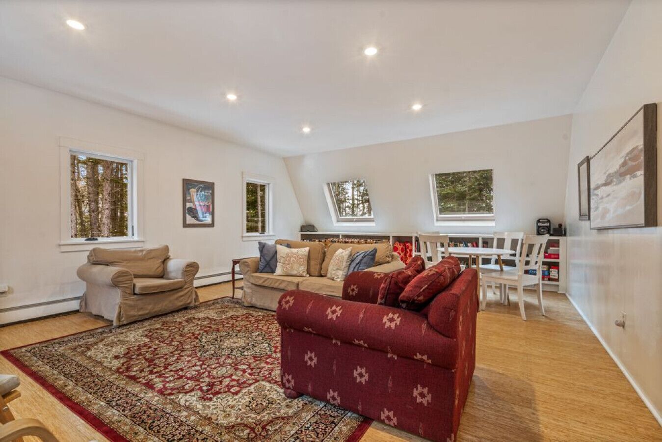 Un salon spacieux avec un canapé rouge, des fauteuils beiges et un tapis à motifs.