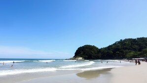 A beach with clear skies, waves, and a distant mountain. - Piscina e AC na Praia do Una (Sao Sebastiao)