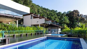 A swimming pool with a blue tiled edge, surrounded by greenery and a building with a balcony. - Piscina e AC na Praia do Una (Sao Sebastiao)