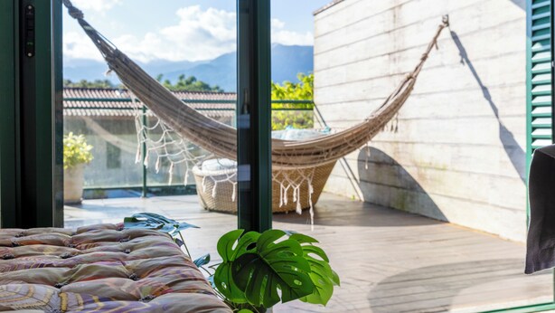 A hammock, a potted plant, and a view of mountains through large windows. - Piscina e AC na Praia do Una (Sao Sebastiao)