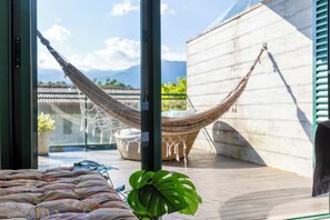 A hammock, a potted plant, and a view of mountains through large windows. - Piscina e AC na Praia do Una (Sao Sebastiao)