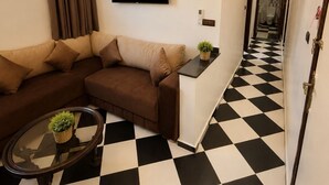 Un salon moderne avec un canapé d’angle, un téléviseur à écran plat, un appareil de climatisation et un sol à carreaux.