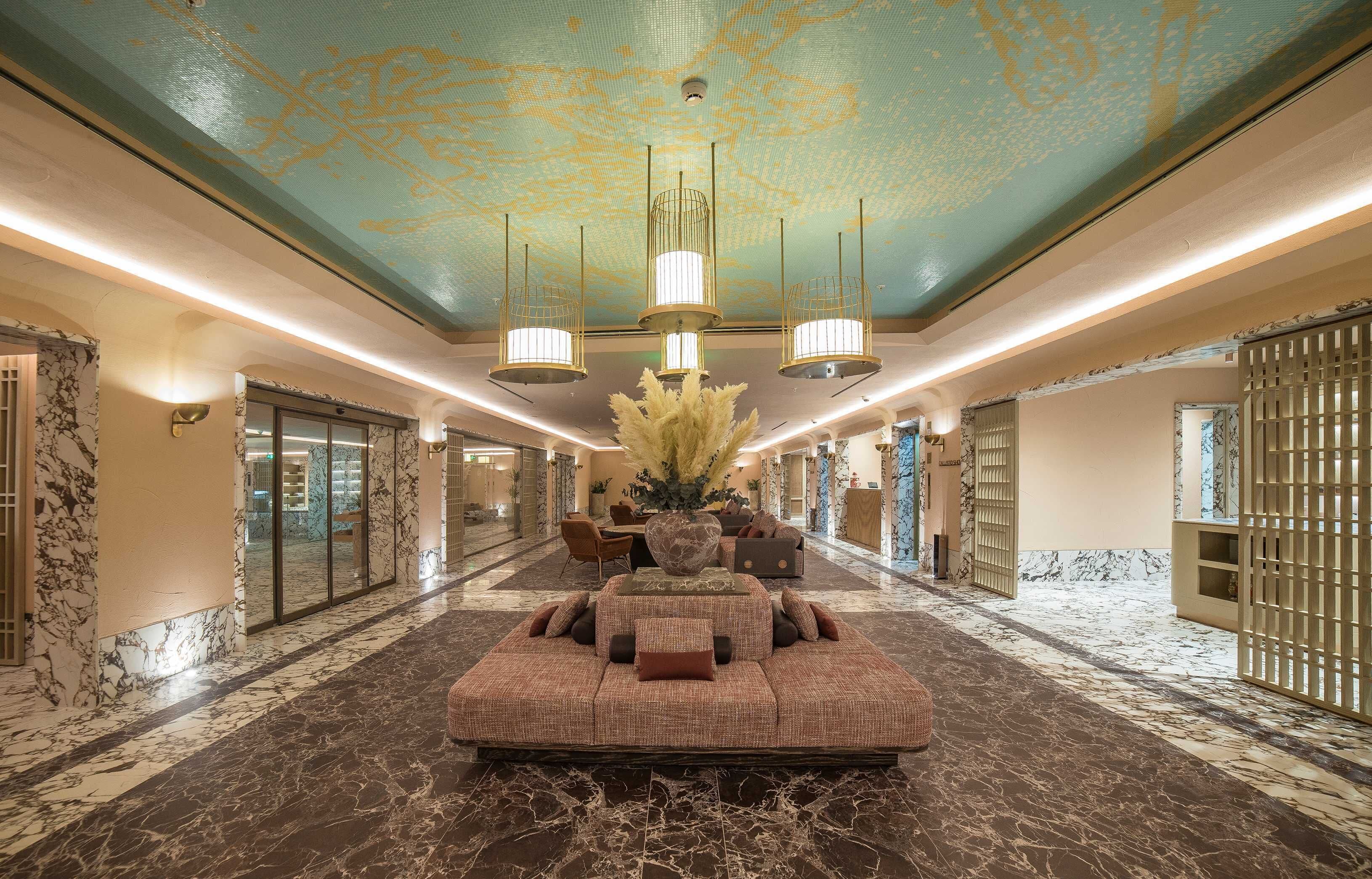A spacious lobby with a large seating area, a decorative ceiling, and marble flooring.