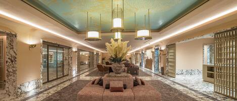 A spacious lobby with a large seating area, a decorative ceiling, and marble flooring.