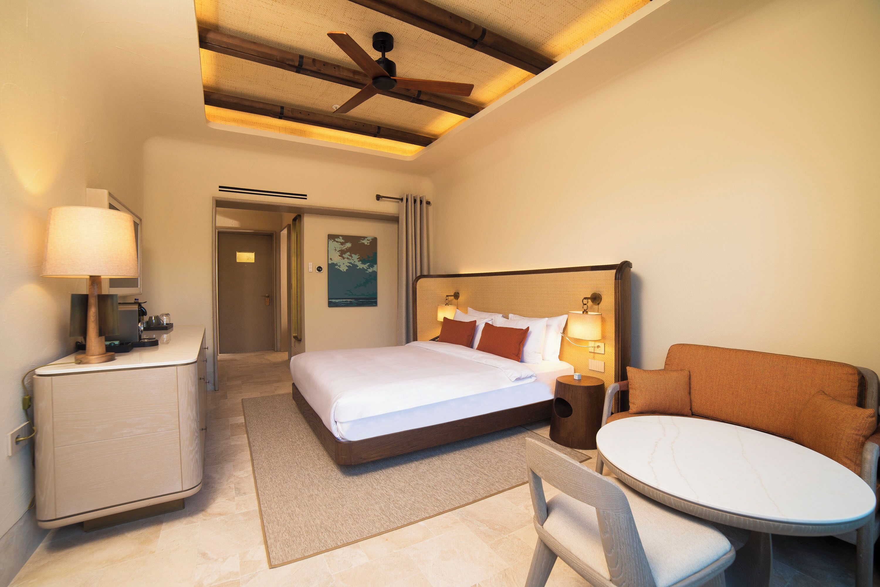 A hotel room with a bed, bedside table, lamp, and a small round table with a chair.