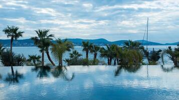 An infinity pool with palm trees and a view of a distant city and mountains.