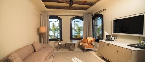A room with a sofa, a dining table with chairs, a TV, and a large window with curtains.