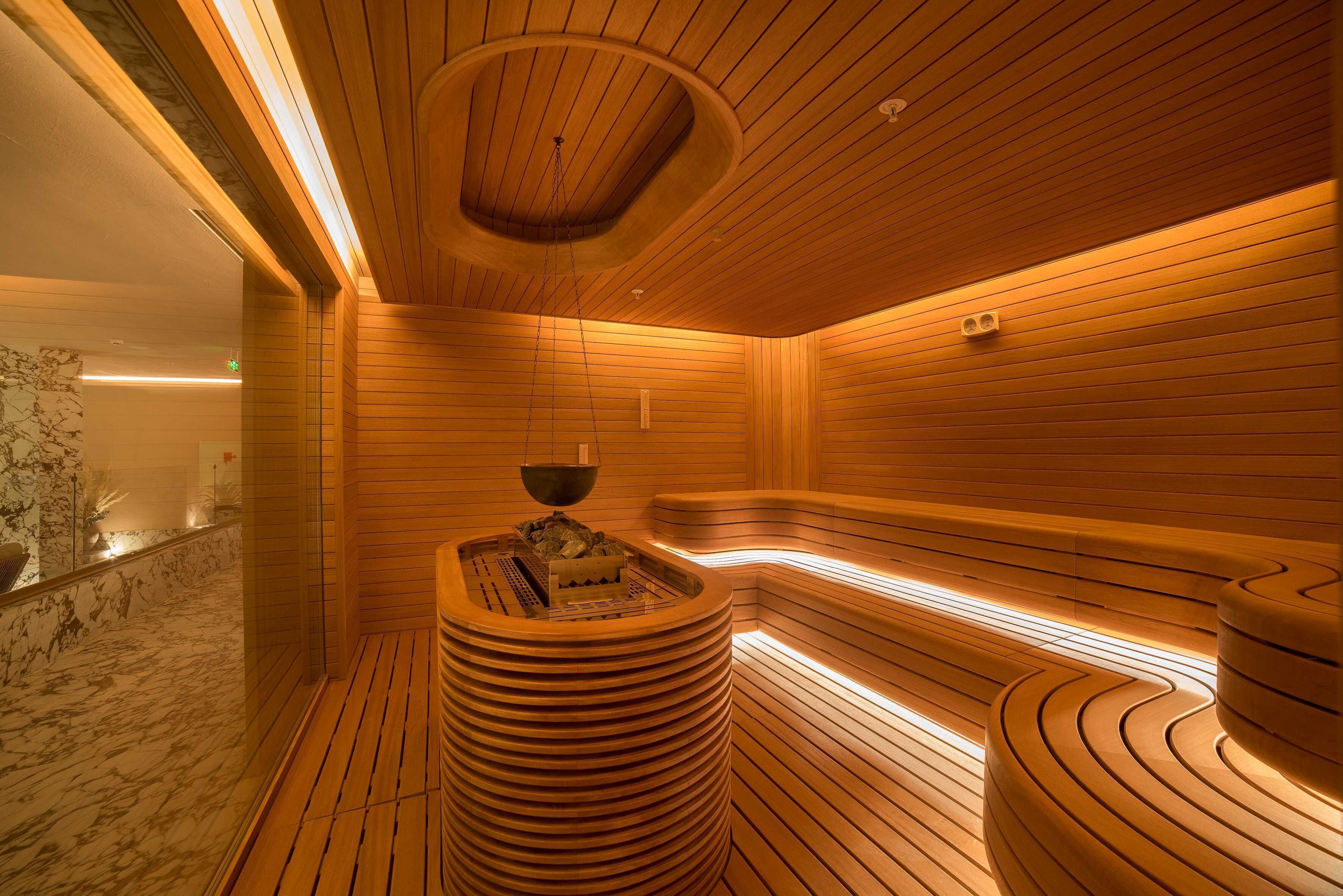 Una sauna con paredes y bancos de madera, suelo de mármol y un elemento calefactor central.