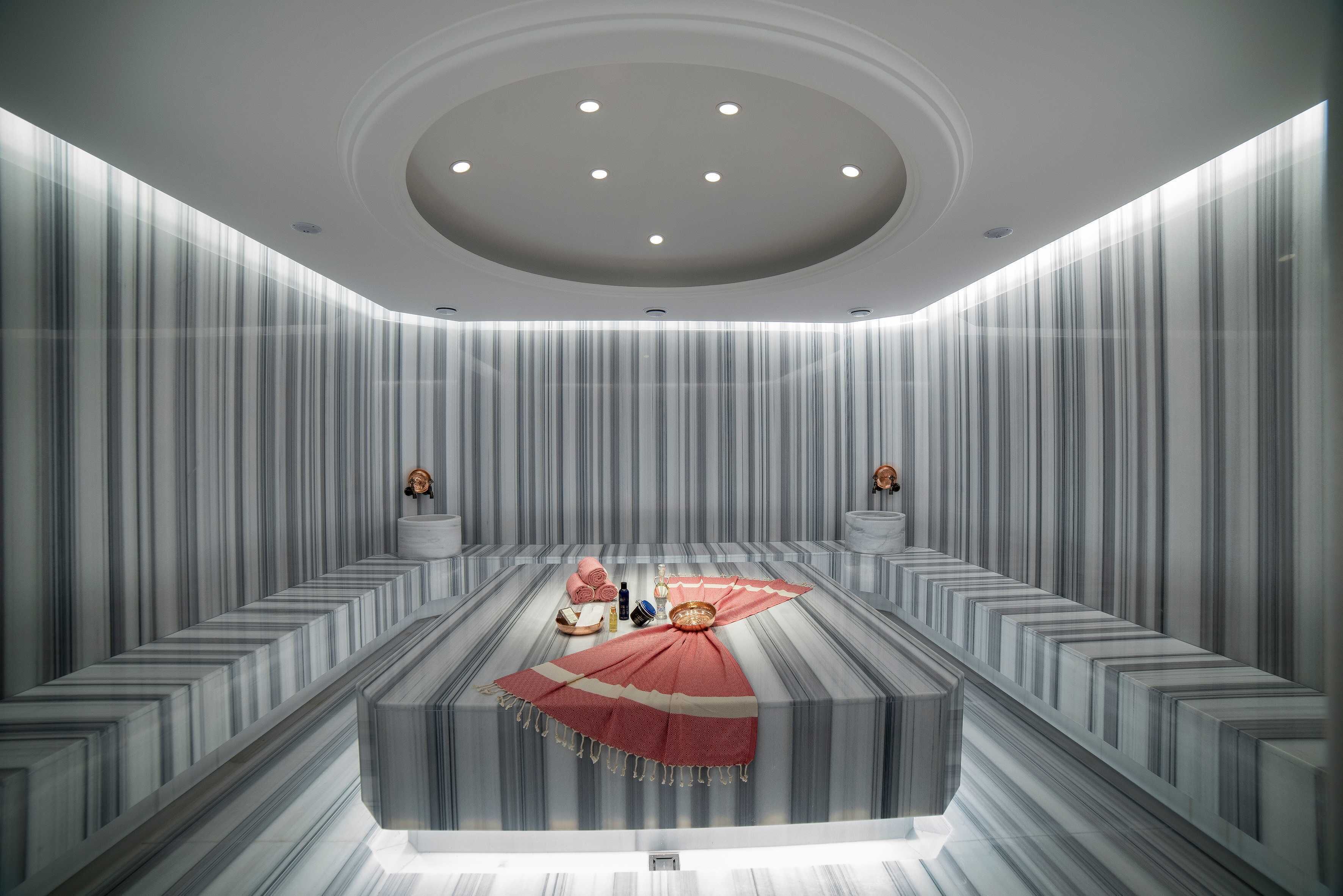 Una habitación de hotel moderna con un mostrador de recepción de mármol, mantel de rayas rojas y blancas, y una lámpara de techo circular.