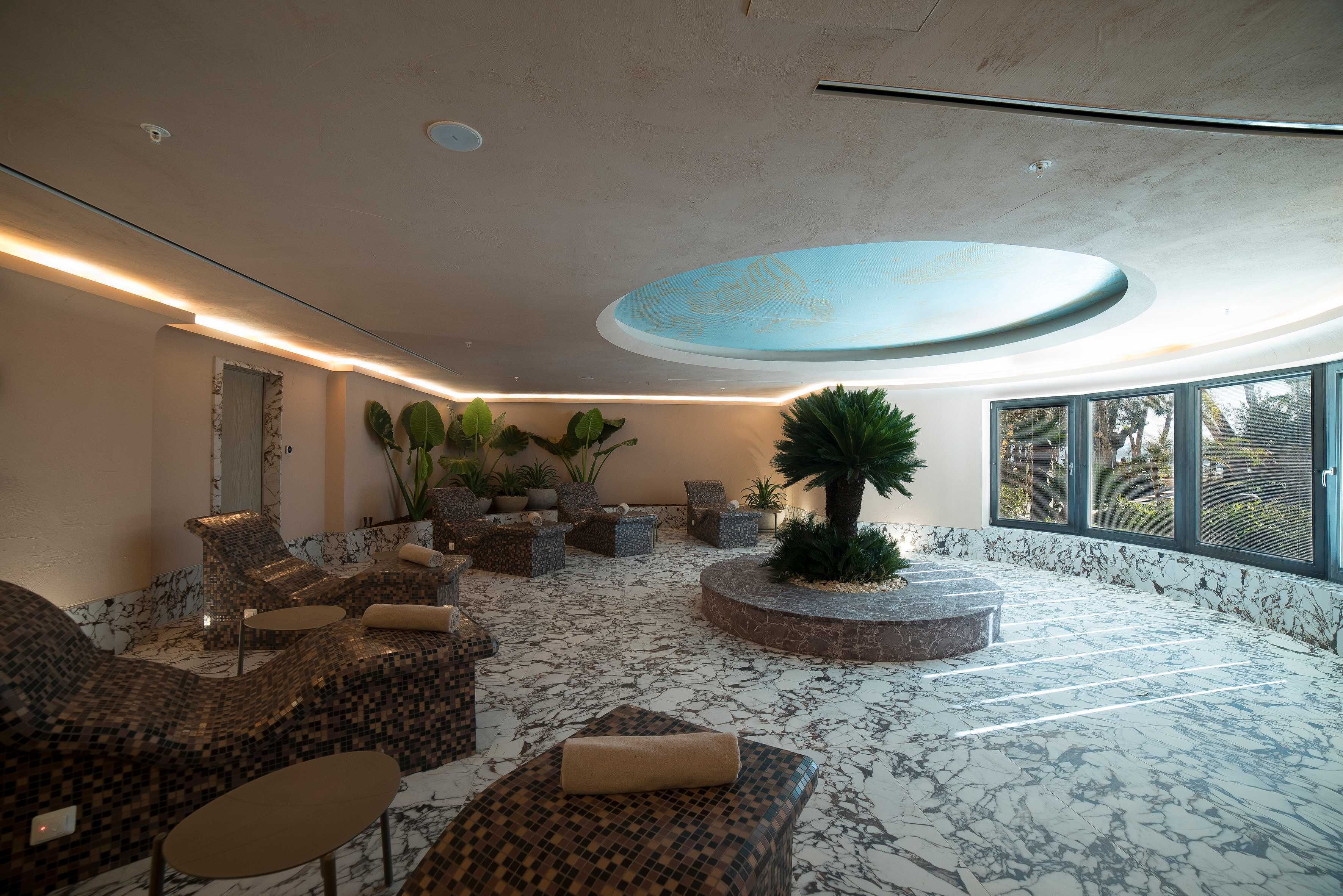 Un espacio interior amplio con disposición de asientos, un elemento decorativo central y ventanas grandes que proporcionan luz natural.