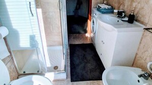Casa de banho com sanita, bidé, máquina de lavar roupa e zona de duche.