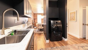 A modern kitchen with a stainless steel sink, a built-in washing machine, and a dining area with a table and chairs. - The Lilliston - Short Stays on Market (Onancock)