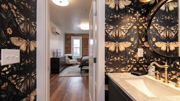 A bathroom with a large mirror, a sink, and a door leading to a bedroom.