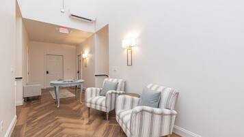 A hallway with a wooden herringbone floor, two striped armchairs, a small round table, and a door in the background.