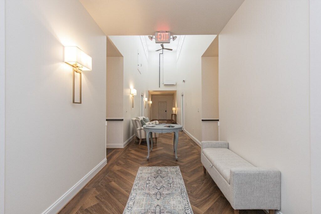 A hallway with a herringbone floor, a light-colored sofa, a small round table, and a patterned rug.