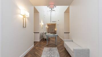 A hallway with a herringbone floor, a light-colored sofa, a small round table, and a patterned rug.