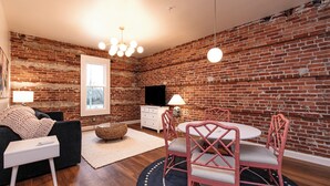 A living room with a brick wall, a round table with chairs, a sofa, a TV, and a lamp.