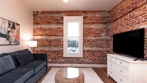 A living room with a brick wall, a sofa, a TV, and a window.