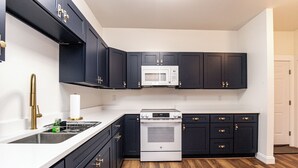 A kitchen with dark cabinets, a white microwave, a stainless steel range hood, and a patterned rug.