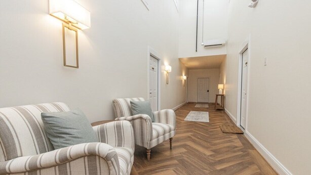 A hallway with striped sofas, a wooden floor, and wall-mounted lights.