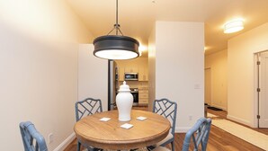 A dining area with a round wooden table, four blue chairs, a white vase, and a hanging light fixture.