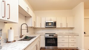 A kitchen with white cabinets, a stainless steel oven, a microwave, and a marble countertop.