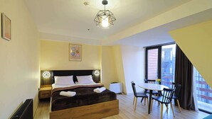 A modern hotel room with a wooden bed, a dining area with a table and chairs, and a large window with a view of the outside. - Comfy Studio in Gudauri Marshall - By Wehost (Gudauri)