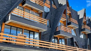 A modern multi-story building with a unique angular design, featuring balconies with wooden railings and large windows. - Comfy Studio in Gudauri Marshall - By Wehost (Gudauri)