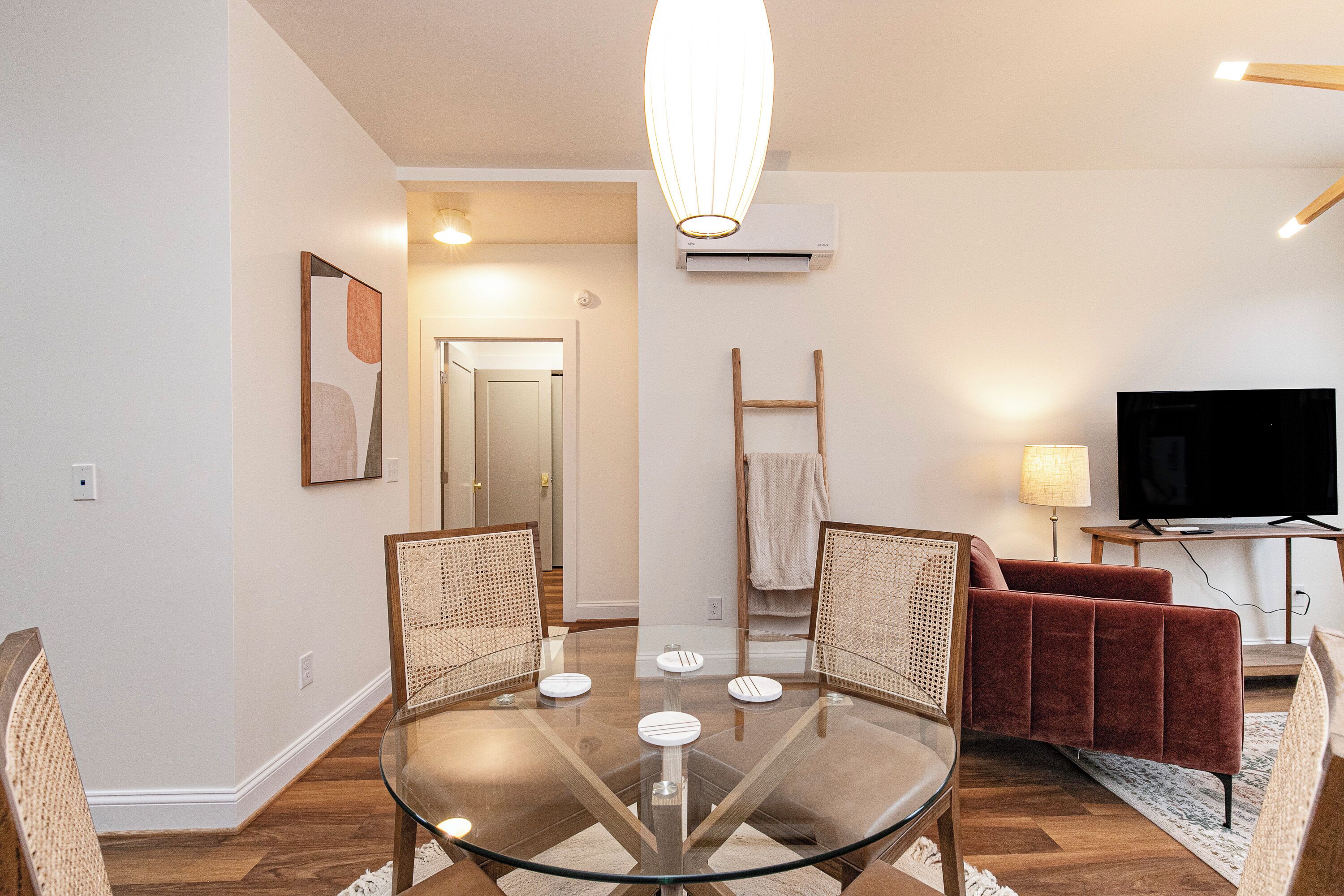 Un salon moderne avec une table à manger au plateau en verre, des chaises en osier, un canapé rouge, un téléviseur à écran plat et une échelle en bois appuyée contre le mur.