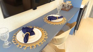 Une table à manger dressée avec des assiettes, des serviettes et de la verrerie, et un téléviseur fixé au mur juste au-dessus.