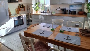 Een moderne keuken met witte kasten, een inbouwoven en een eethoek met een houten tafel en stoelen.