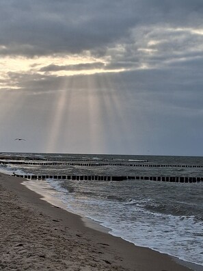 Ein Strand mit Wellen, einem Steg und einem bewölkten Himmel.