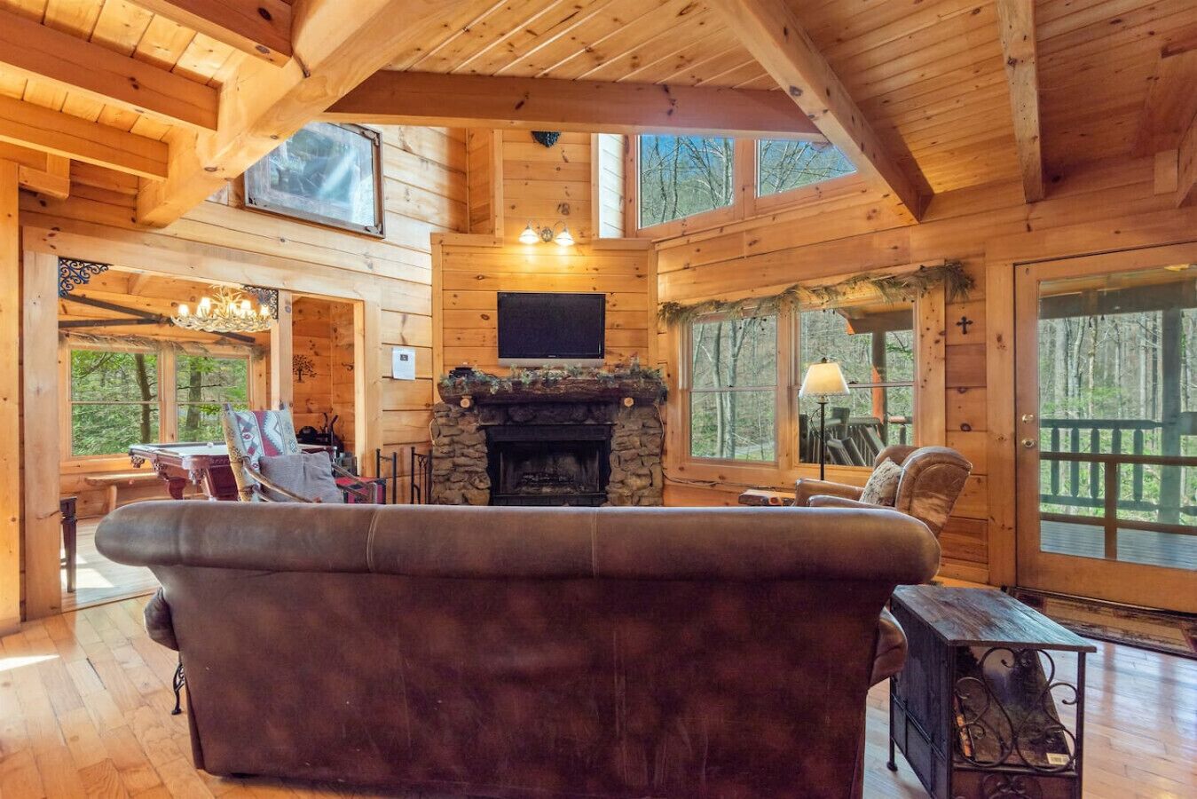A cozy cabin interior with a stone fireplace, wooden walls, and large windows offering views of the forest.