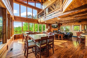 A spacious wooden cabin with a large dining area, a cozy living room, and a balcony overlooking a forested area. - 7BR w/Incredible Views! Hot Tub*Game Room*Resort (Sevierville)