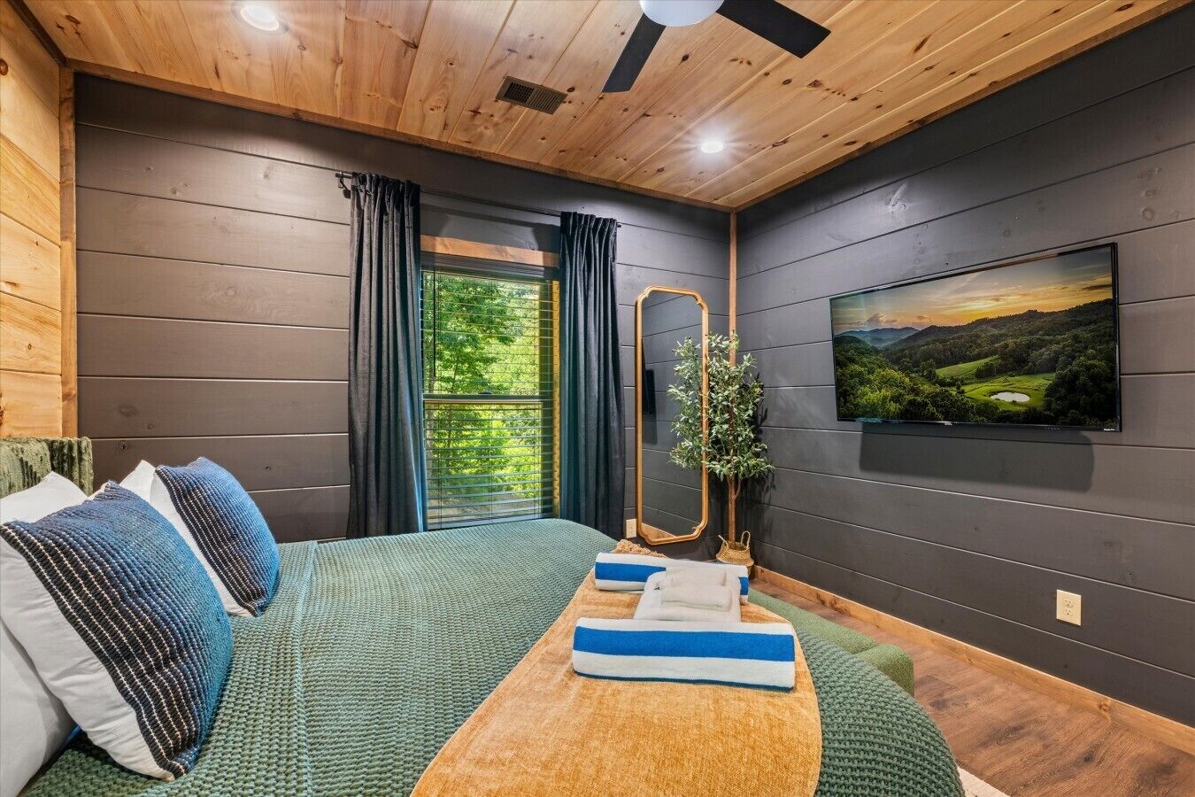 A bedroom with a bed, a TV, a window, and a mirror.