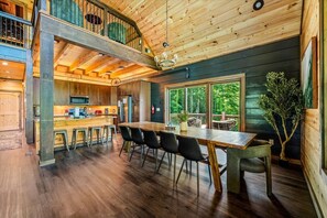 A spacious wooden cabin with a dining area, kitchen, and a loft bedroom. - Luxe 4BR Pool Cabin*Hot Tub*Firepit*Games*Theater! (Sevierville)