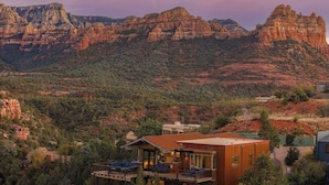 Um edifício moderno de dois andares com varanda, rodeado por árvores e montanhas.