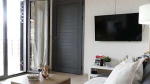 En moderne stue med sofa, sofabord og et fladskærms-tv på væggen.
