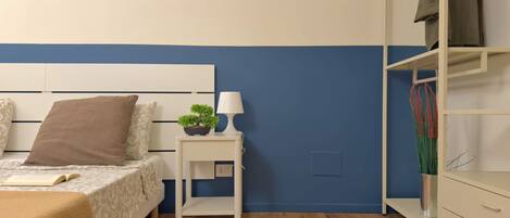 A bedroom with a bed, bedside table with a lamp, a small potted plant, and a wardrobe.