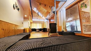 A spacious room with wooden walls and ceiling, a large window with a view, and a seating area with patterned cushions. - La Cedar Villa by Staycation (Manali)