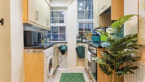 Una cocina compacta con armarios de madera, lavadora, microondas y una planta verde.