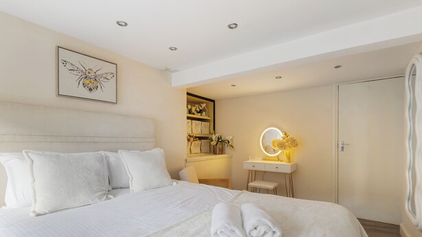 Una habitación de hotel con una cama grande, una mesita de noche con espejo, un escritorio pequeño y un armario.