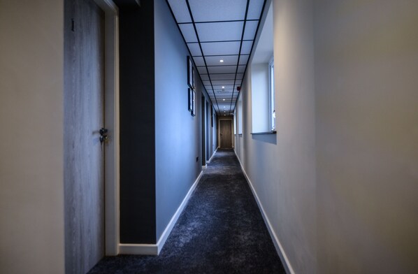 Een smalle gang met vloerbedekking, een plafond met inbouwspots en deuren aan beide kanten.