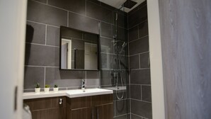 A modern bathroom with dark tiles, a white sink, a mirror, and a glass-enclosed shower. - Ladywell House (Birmingham)