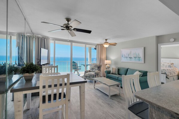 A spacious living area with a balcony overlooking the sea, a dining table, and a sofa. - Relax, Unwind & Soak Up the Sun – Direct Beachfront Condo, W/Beach Chair Service (Panama City Beach)