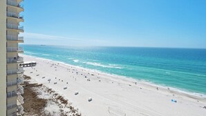 Een strand met een helder uitzicht op de oceaan, een zandstrand en een gebouw met balkons dat uitkijkt over het strand.