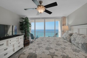 A bedroom with a bed, a TV, a dresser, a plant, and a view of the ocean. - Relax, Unwind & Soak Up the Sun – Direct Beachfront Condo, W/Beach Chair Service (Panama City Beach)
